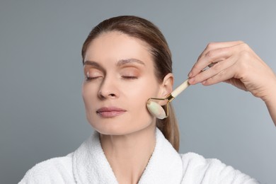 Woman massaging her face with jade roller on grey background