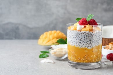 Delicious chia pudding with mango, raspberries and granola on light grey table, space for text