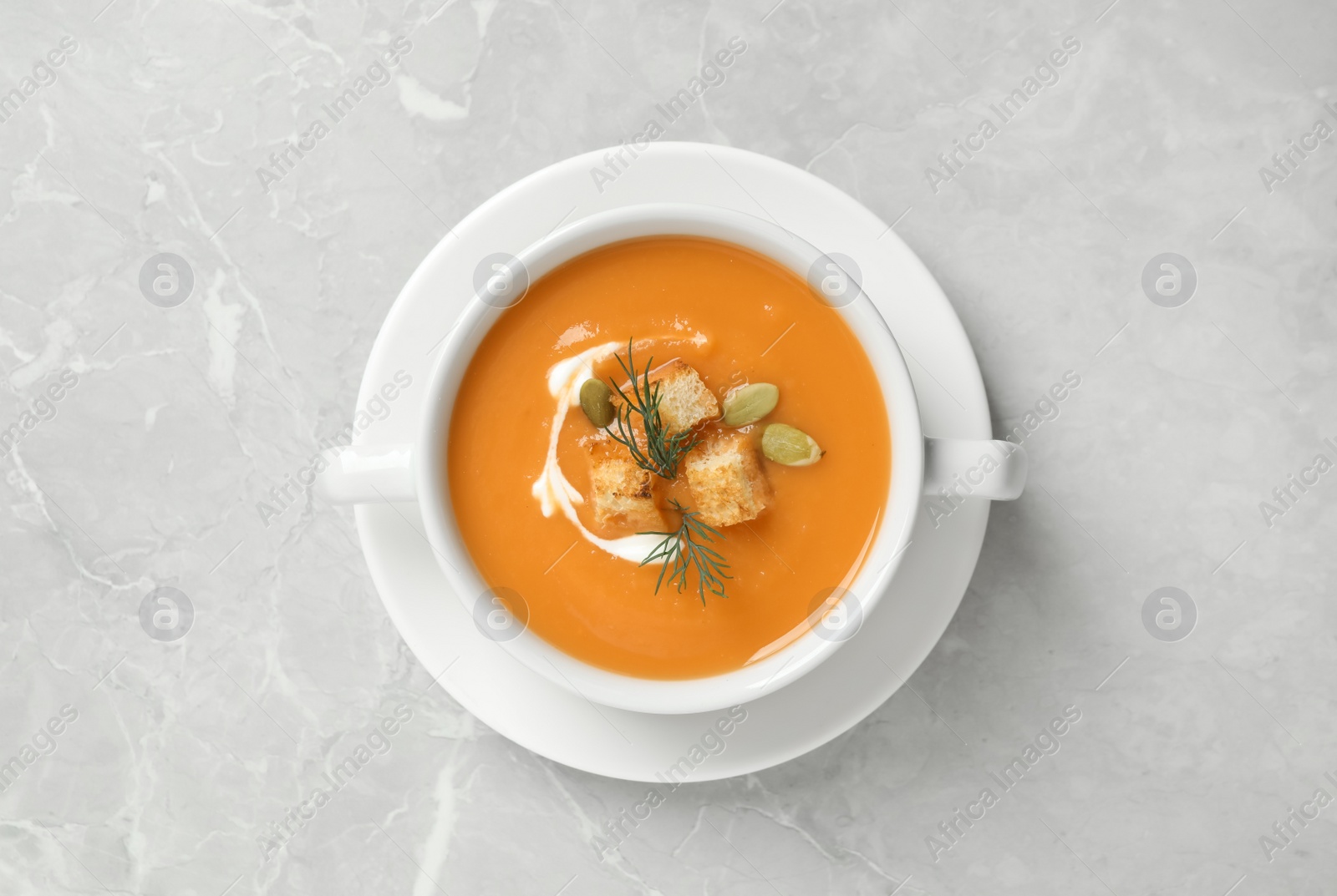 Photo of Tasty creamy pumpkin soup with croutons, seeds and dill in bowl on light grey table, top view