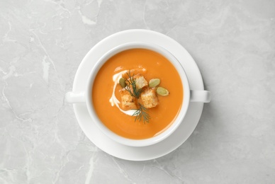 Photo of Tasty creamy pumpkin soup with croutons, seeds and dill in bowl on light grey table, top view