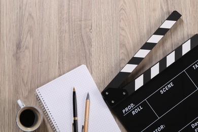 Movie clapper, notebook, coffee and pens on wooden table, flat lay. Space for text