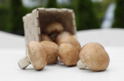 Photo of Overturned basket with fresh champignon mushrooms on white table outdoors, closeup