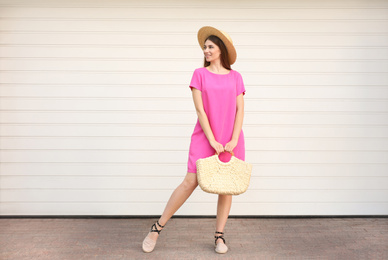 Beautiful young woman with stylish straw bag near white wall outdoors