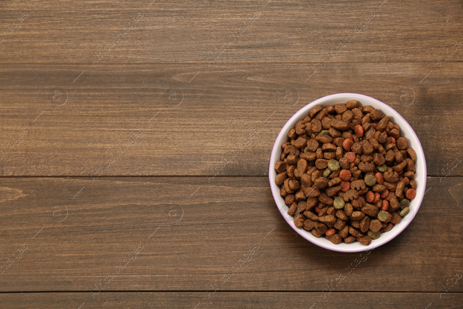 Photo of Dry food in pet bowl on wooden background, top view. Space for text