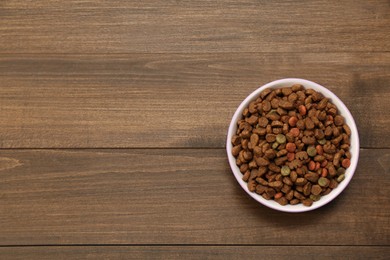 Photo of Dry food in pet bowl on wooden background, top view. Space for text