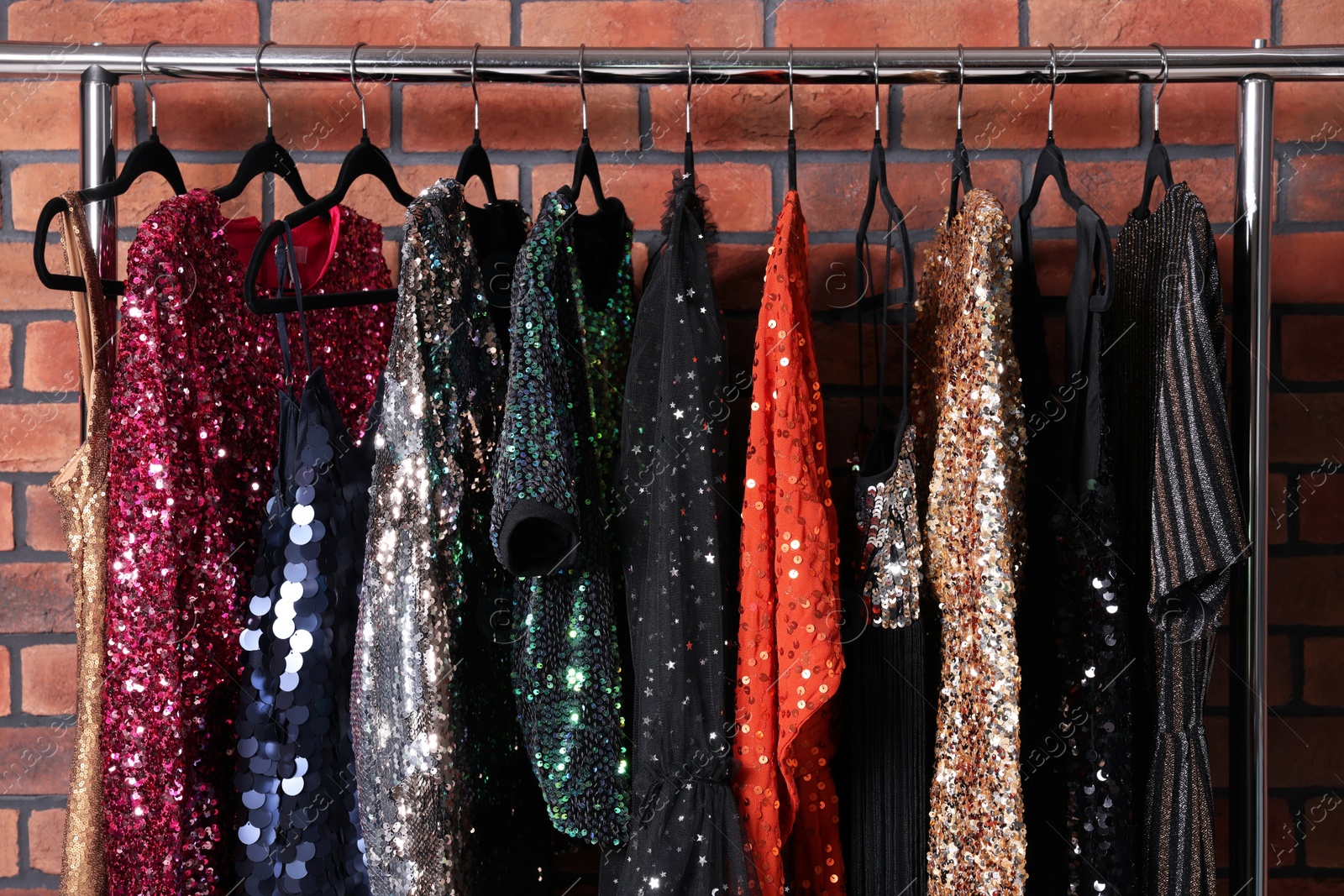 Photo of Rack with collection of fashionable dresses near brick wall in showroom. Preparing for party