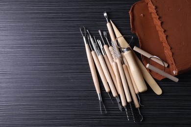 Photo of Clay and set of modeling tools on dark gray wooden table, flat lay. Space for text