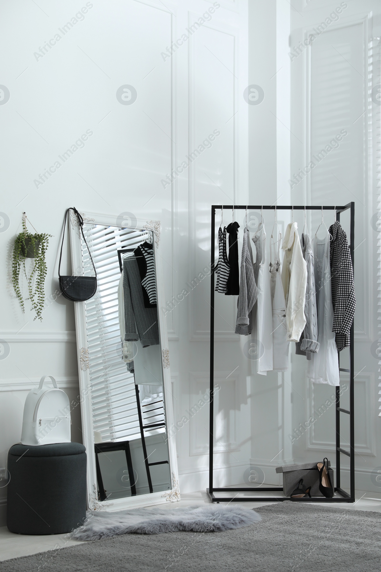 Photo of Rack with stylish women's clothes and large mirror in dressing room. Interior design