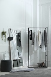 Rack with stylish women's clothes and large mirror in dressing room. Interior design