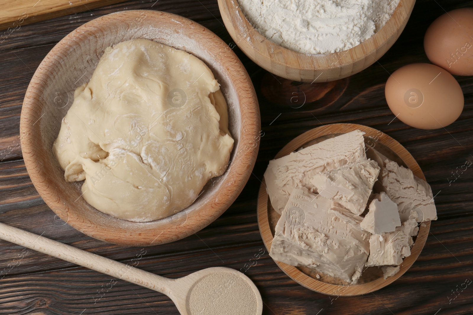 Photo of Different types of yeast, eggs, flour and dough on wooden table, flat lay