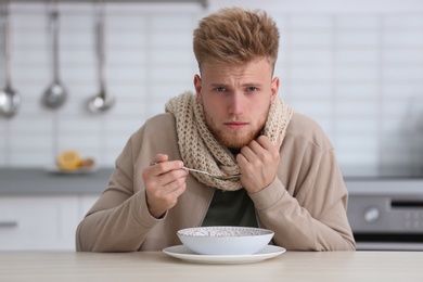 Photo of Sick young man eating soup to cure flu at table in kitchen