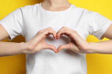 Photo of Woman making heart with hands on yellow background, closeup