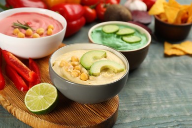 Photo of Different kinds of tasty hummus with ingredients on light blue wooden table