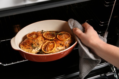 Woman taking delicious lemon chicken out of oven, closeup