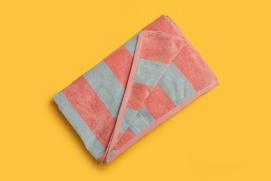 Folded striped beach towel on yellow background, top view