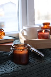 Photo of Burning candle in jar on knitted plaid near window indoors, space for text