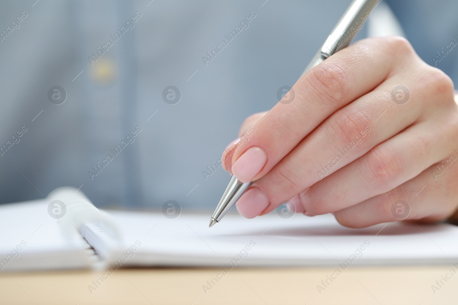 Photo of Woman writing with pen in notebook at wooden table, closeup