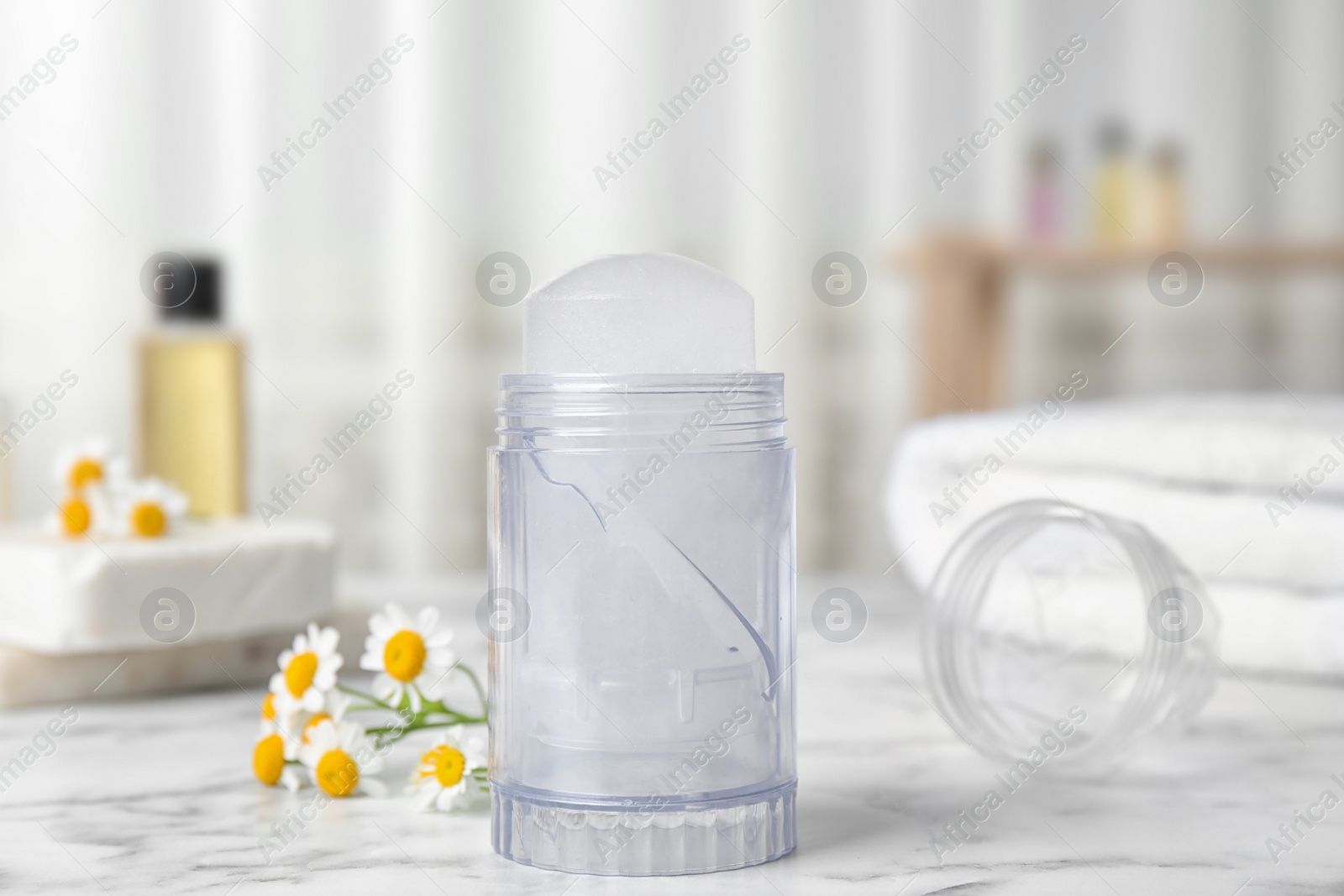 Photo of Natural crystal alum deodorant and chamomile flowers on white marble background