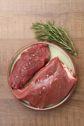 Photo of Pieces of raw beef meat with spices and rosemary on wooden table, flat lay