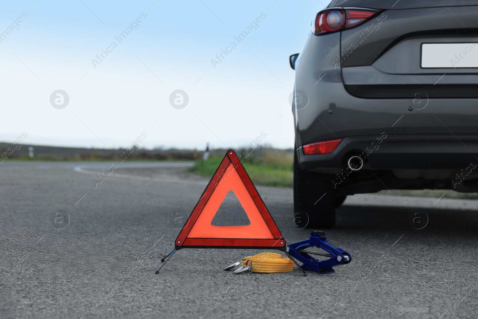 Photo of Emergency warning triangle, towing strap and scissor jack near car outdoors. Safety equipment