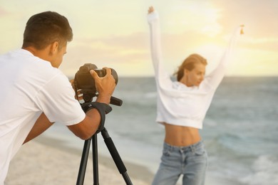 Photographer taking picture of model with professional camera near sea