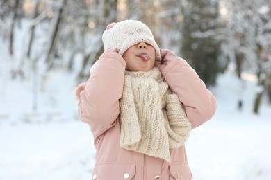 Photo of Cute little girl showing her tongue in snowy park on winter day