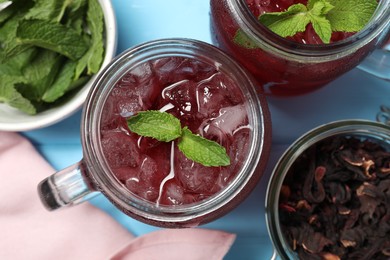 Photo of Delicious iced hibiscus tea with mint and dry flowers on light blue table, flat lay