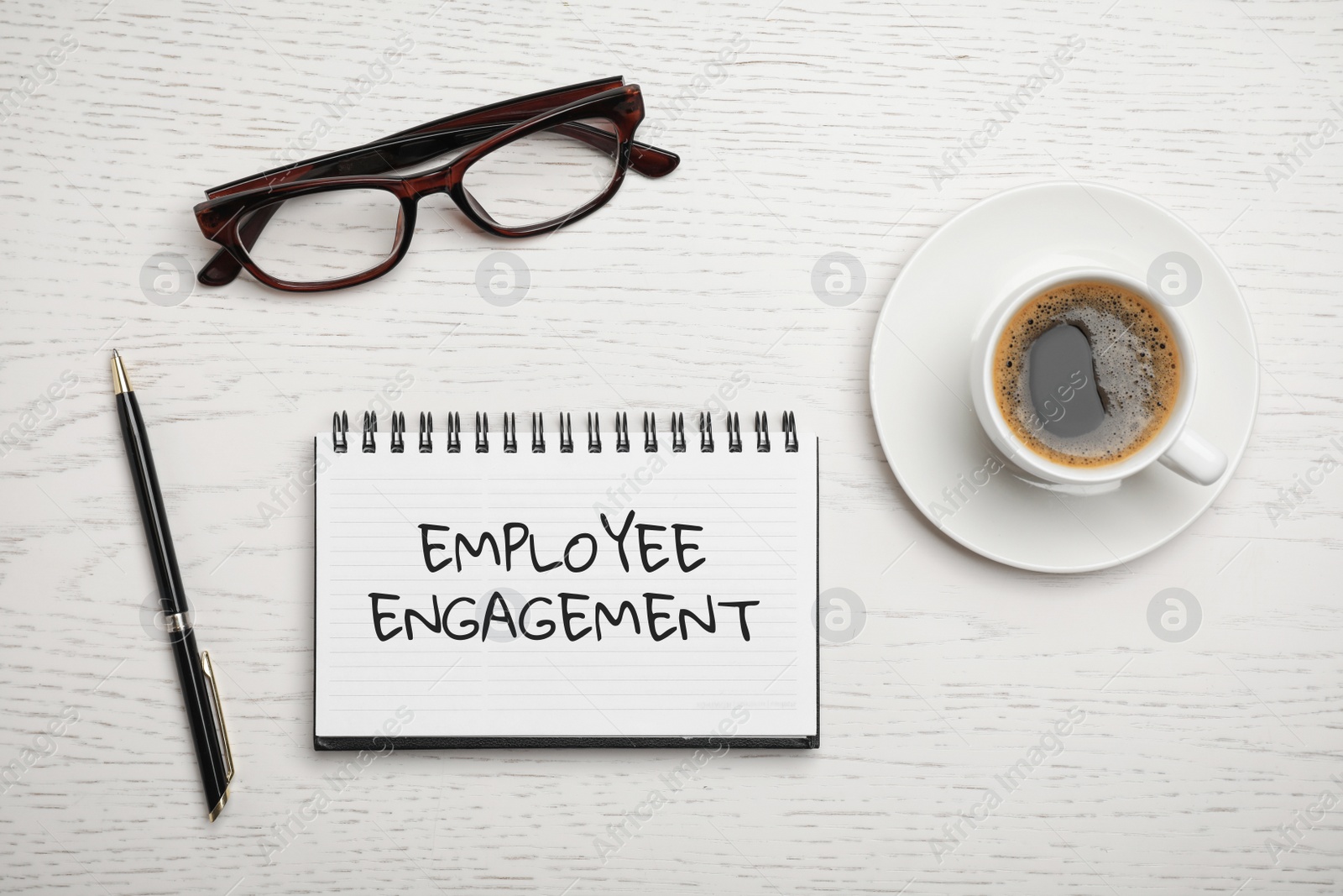 Image of Notebook with text EMPLOYEE ENGAGEMENT, glasses and cup of coffee on table, flat lay