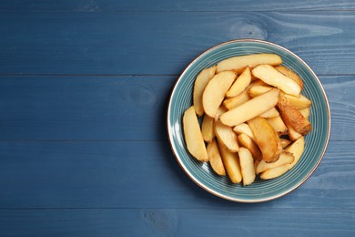 Photo of Plate with delicious baked potatoes on blue wooden table, top view. Space for text
