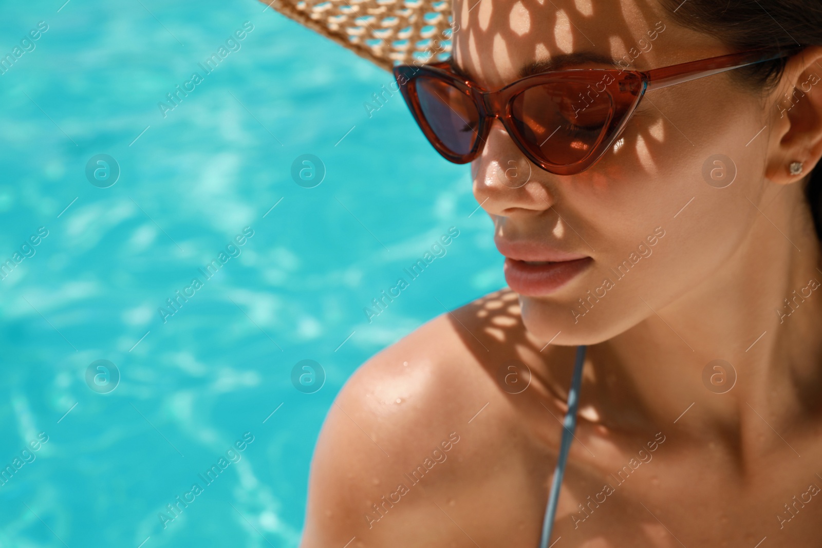 Photo of Beautiful woman wearing hat and sunglasses in swimming pool, closeup. Space for text