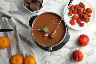 Photo of Flat lay composition with chocolate fondue and strawberries in pot on marble background