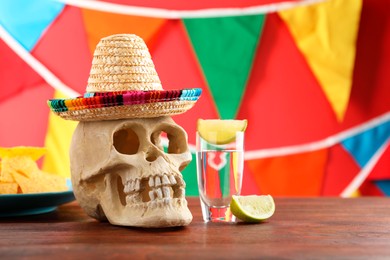 Human scull with Mexican sombrero hat and tequila on wooden table. Space for text