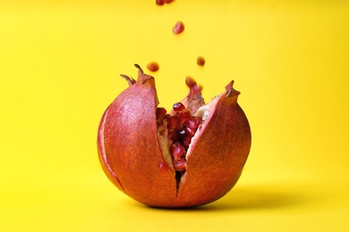 Photo of Delicious red ripe pomegranate and falling seeds on color background