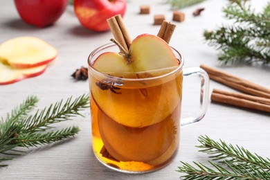 Photo of Hot mulled cider and fir branches on white wooden table, closeup