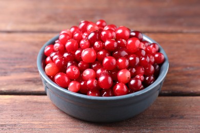 Photo of Fresh ripe cranberries in bowl on wooden table, closeup