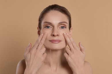 Woman massaging her face on beige background