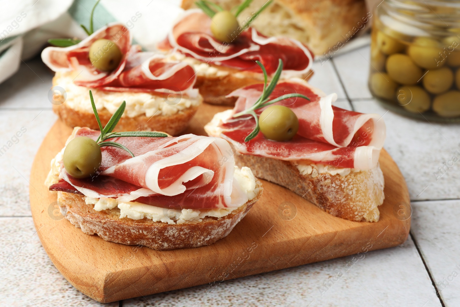 Photo of Tasty sandwiches with cured ham, rosemary and olives on tiled table, closeup