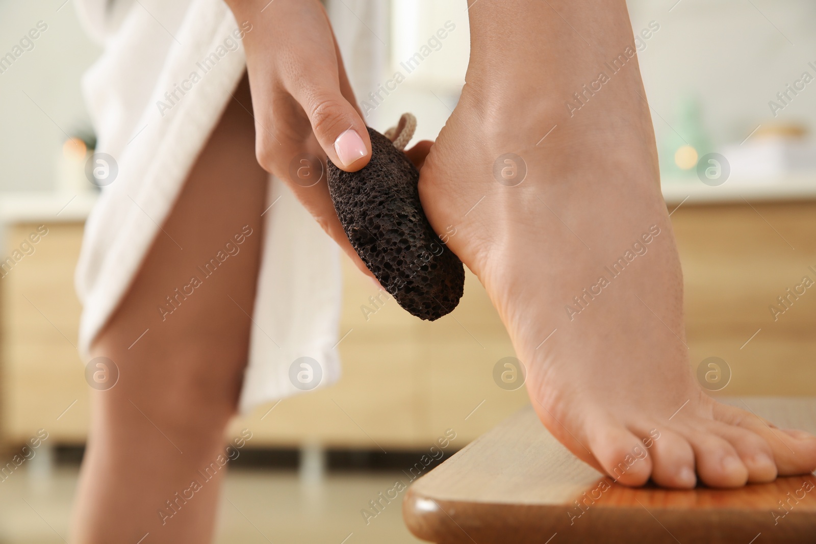 Photo of Woman using pumice stone for removing dead skin from feet in bathroom, closeup