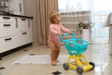 Photo of Cute baby with toy walker in kitchen near window. Learning to walk