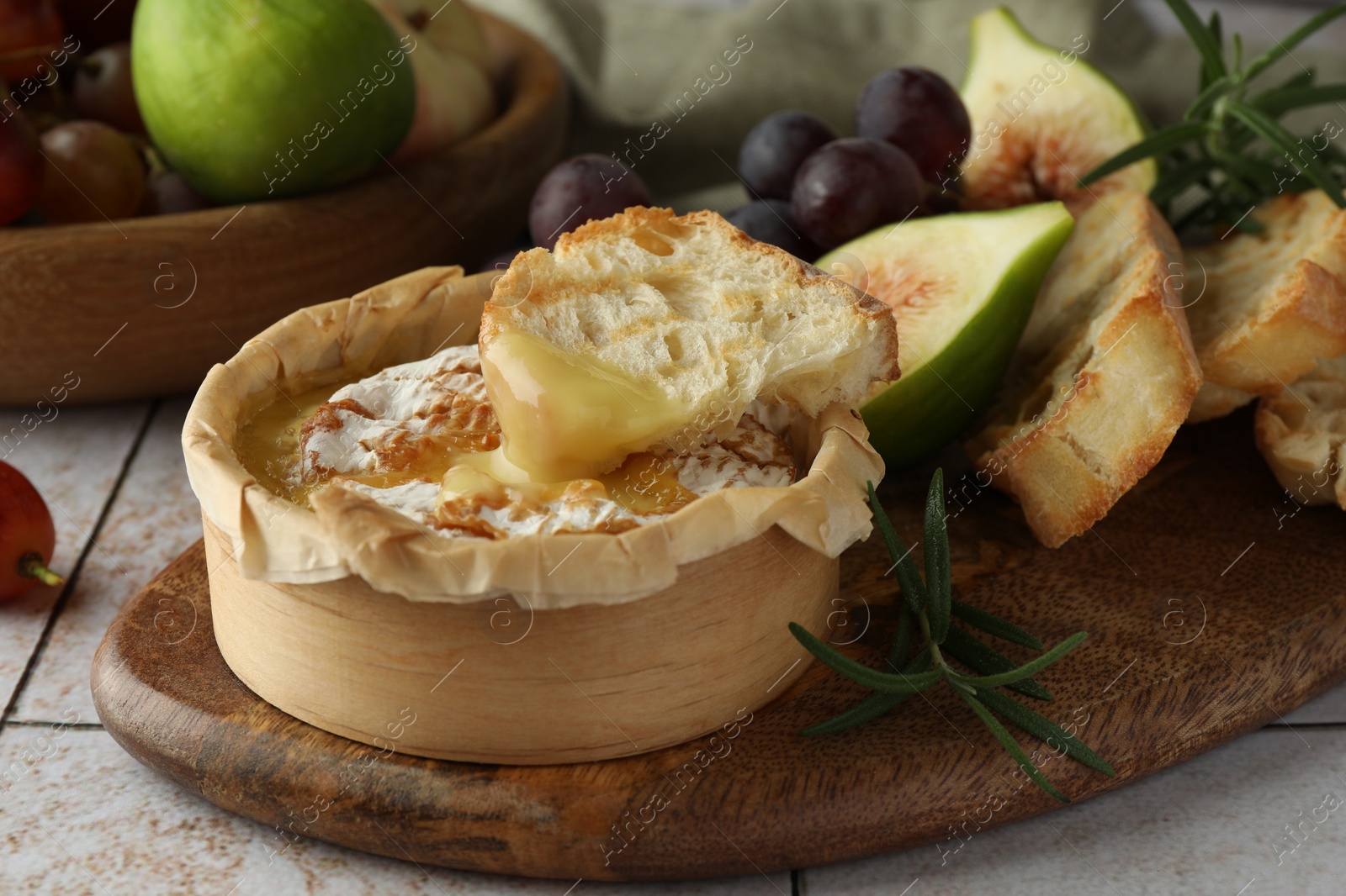 Photo of Tasty baked brie cheese, bread and other products on light tiled table