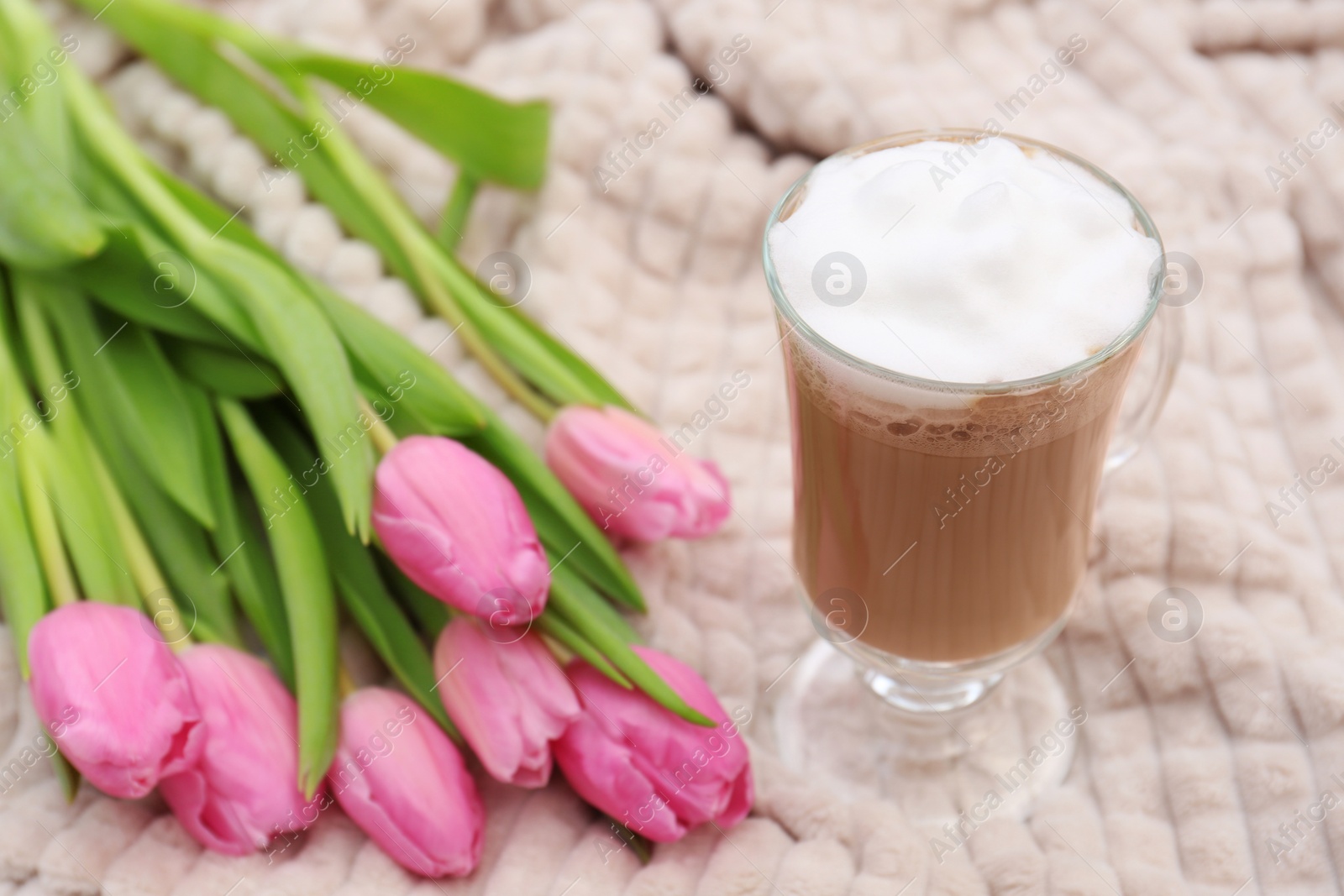 Photo of Glass of delicious cocoa and pink tulips on light blanket, closeup