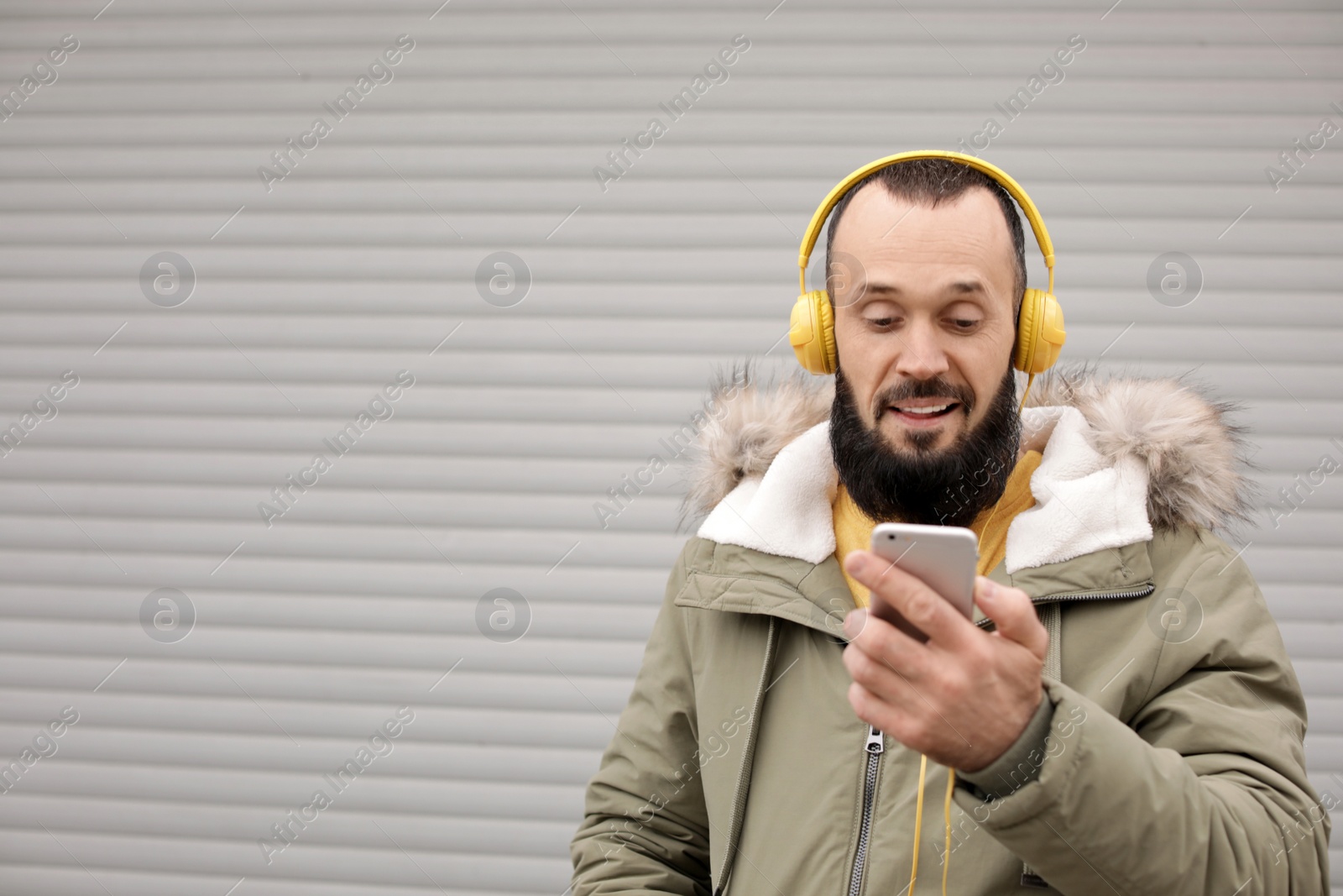 Photo of Mature man with headphones listening to music near light wall. Space for text