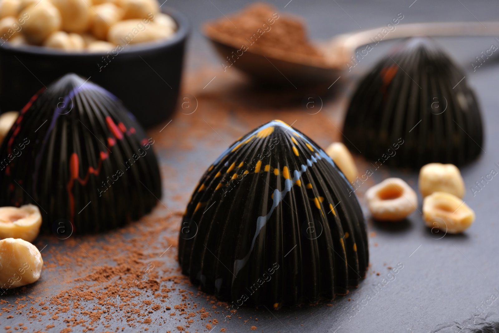 Photo of Tasty chocolate candies and nuts on slate plate, closeup