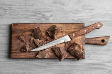 Pieces of delicious dark chocolate and knife on wooden board, top view