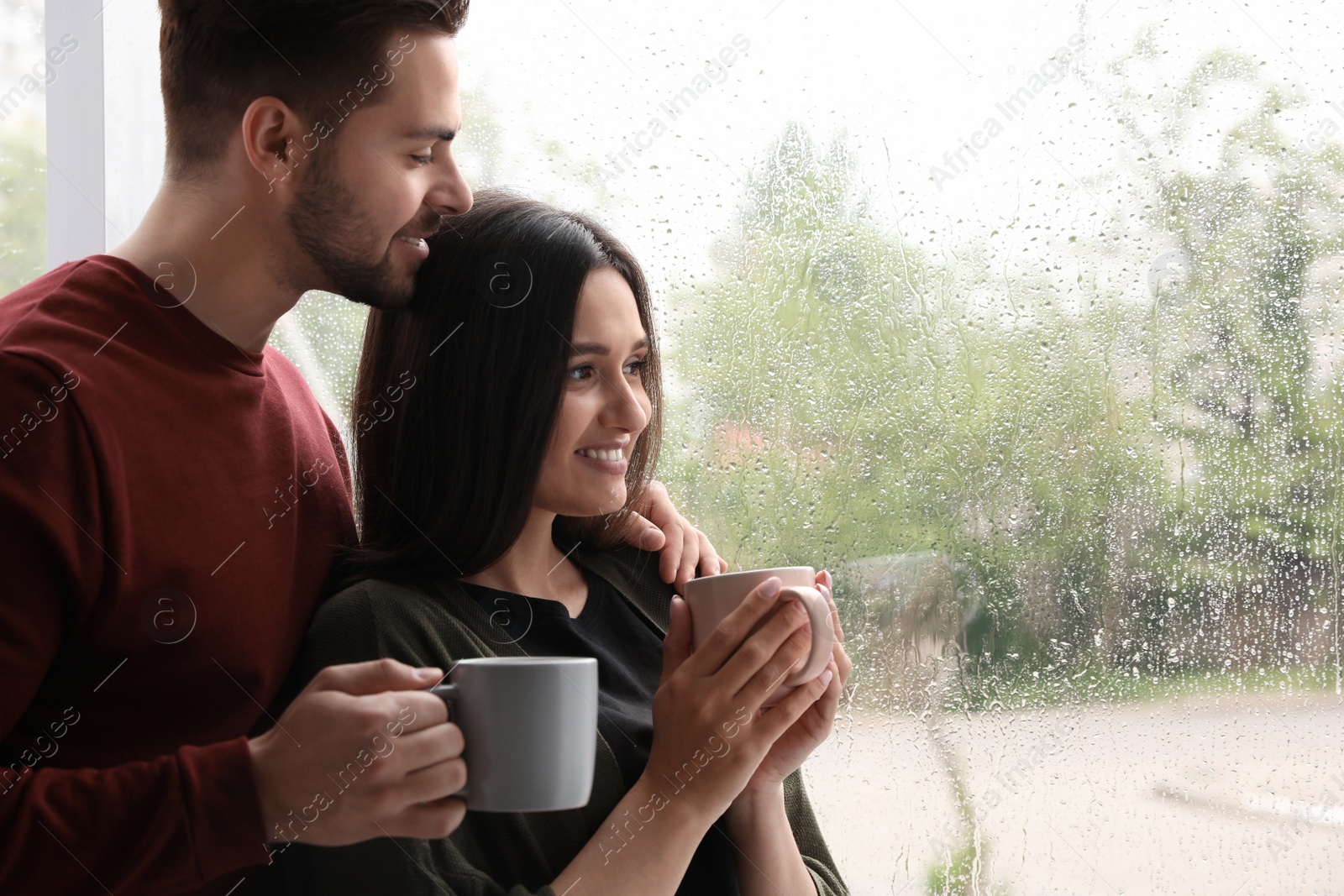 Photo of Happy young couple near window indoors on rainy day