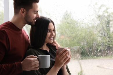 Photo of Happy young couple near window indoors on rainy day