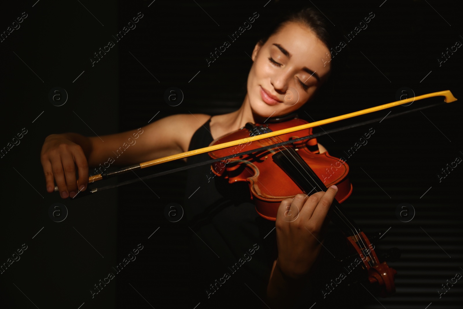 Photo of Beautiful young woman playing violin in dark room, focus on hand