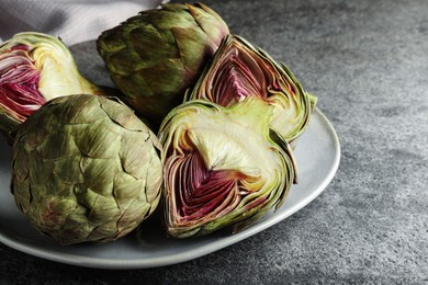 Photo of Cut and whole fresh raw artichokes on grey table, closeup