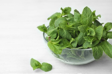 Glass bowl with fresh green mint on table. Space for text