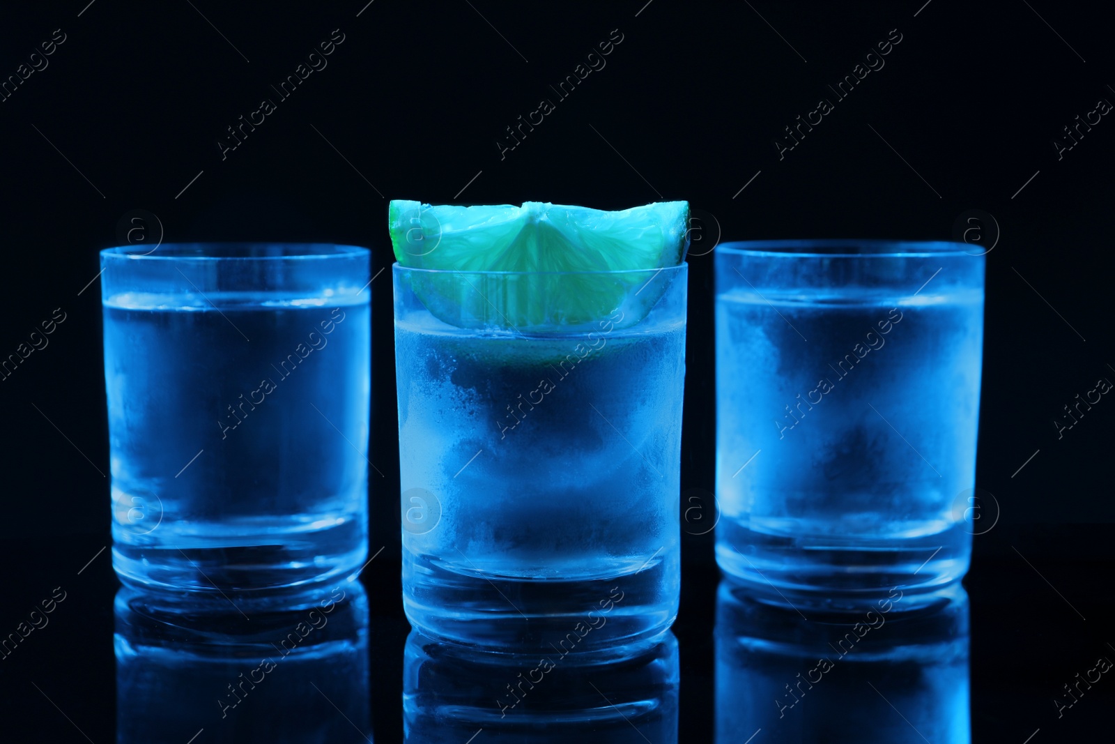 Photo of Shot glasses of vodka with lime slice on dark background